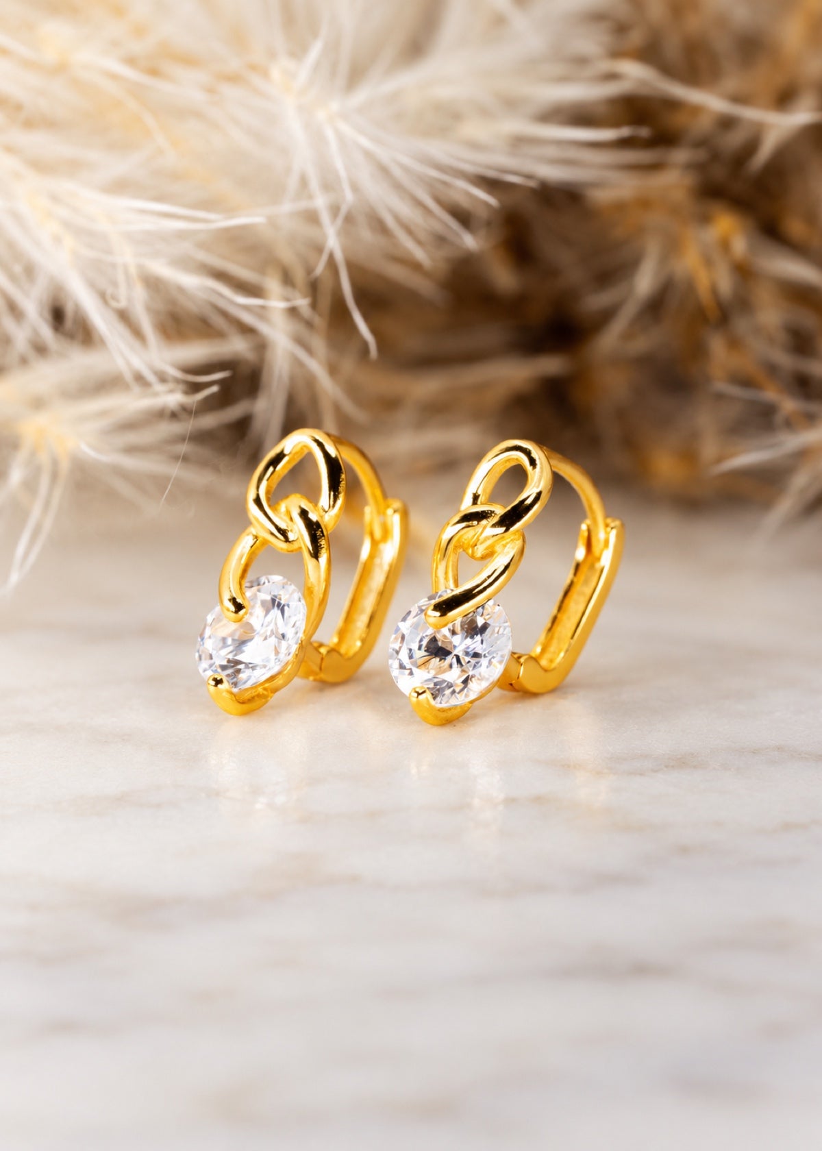 Gold Twisted Chain huggies on marble beside dried grass
