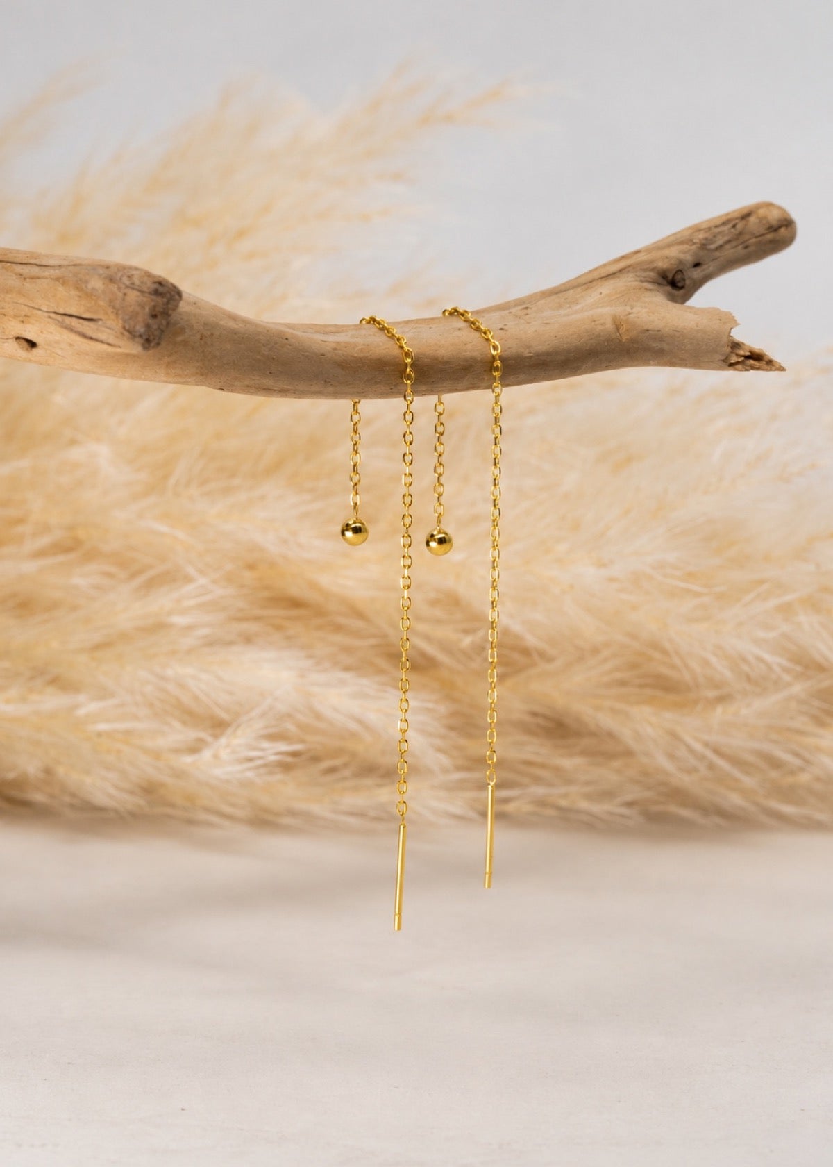 Ball threader earrings hanging from a branch to show chain length