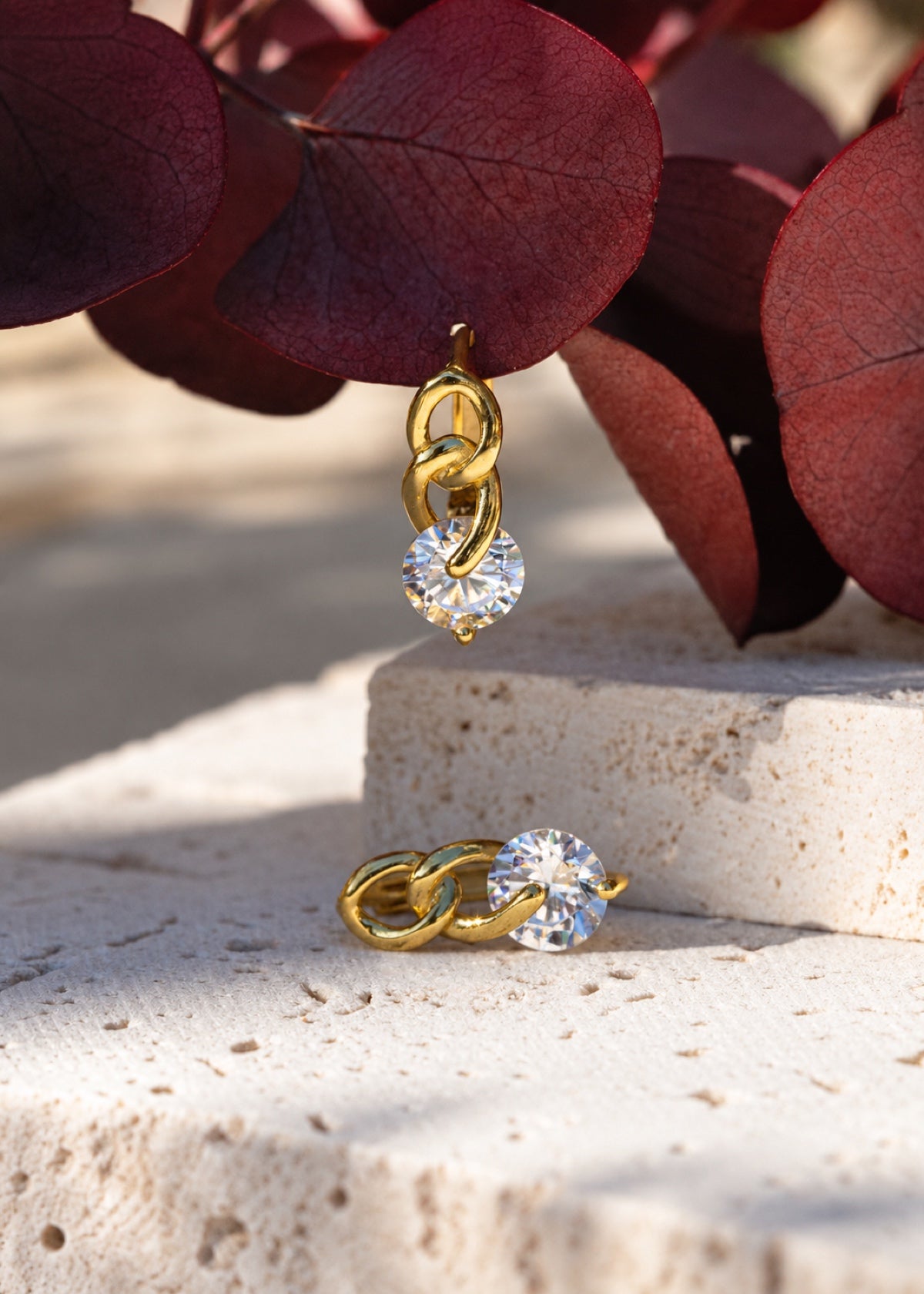 Twisted Chain huggies arranged on a stone block and purple leaves