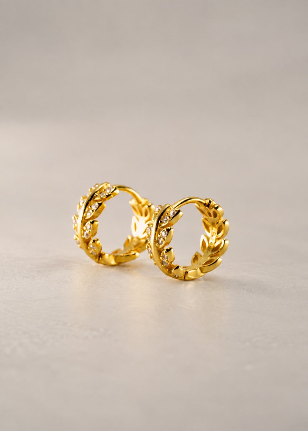 Gold Olive Leaf huggies displayed upright on a stone surface