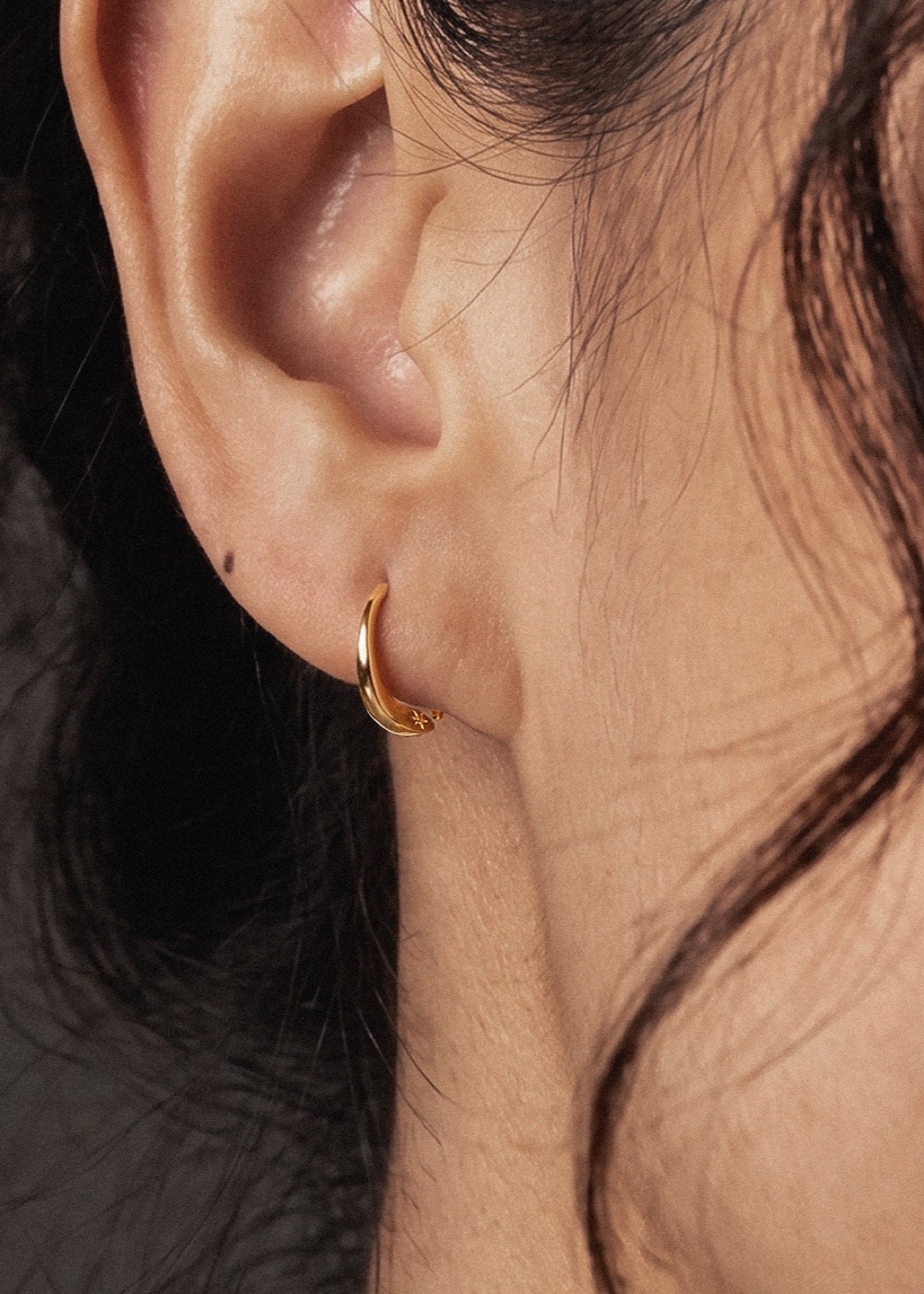 Single gold D Shape sleeper earring worn in an earlobe