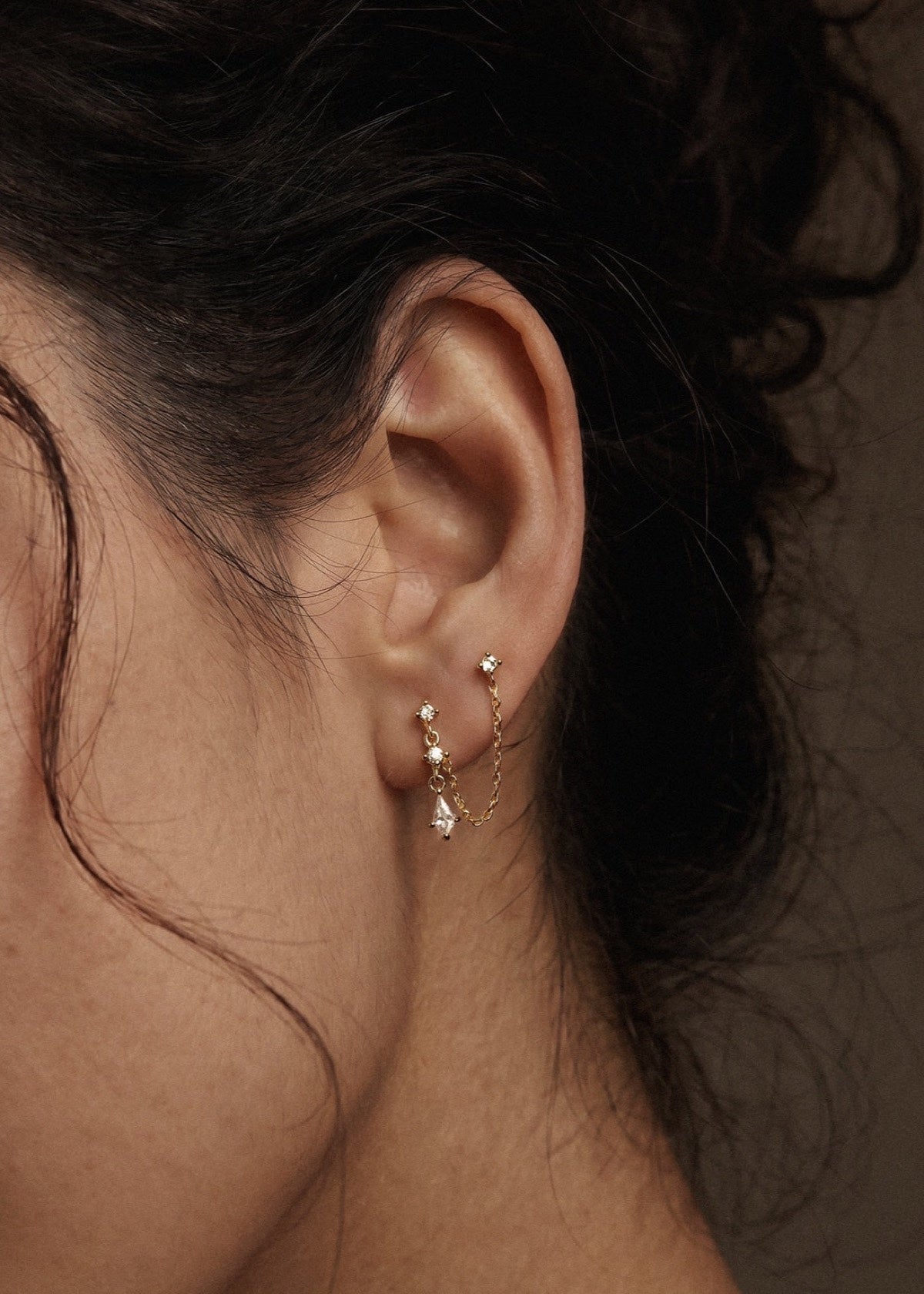 Gold double-piercing chain earring styled beside dark hair
