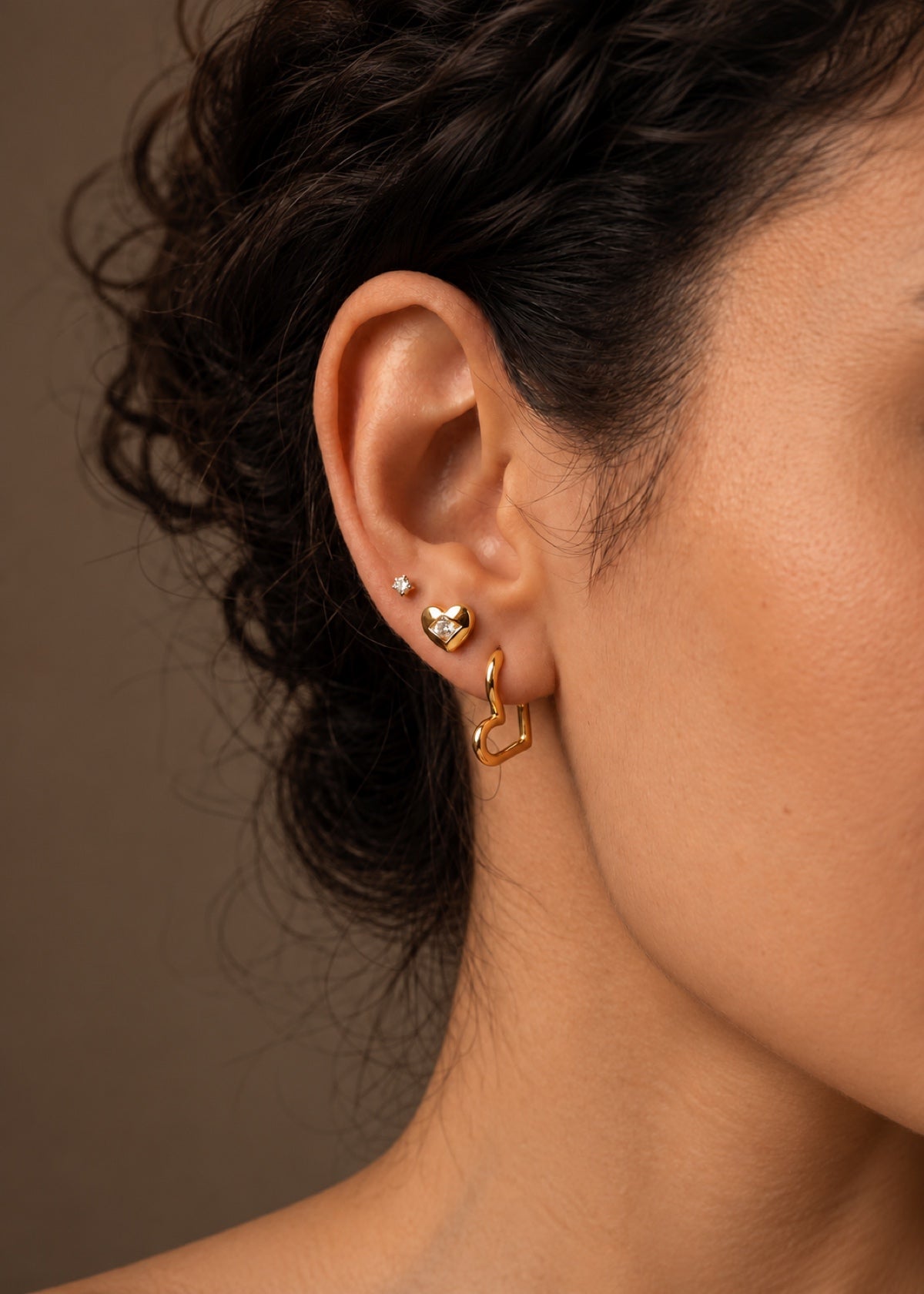 Side view of gold heart studs and huggies worn together