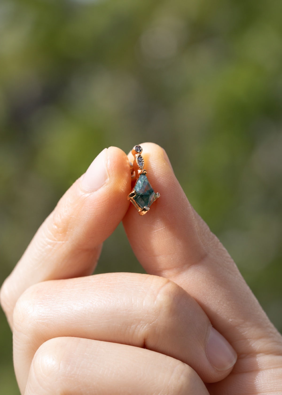 Hand holding a moss agate earring to show its green stone and gold setting