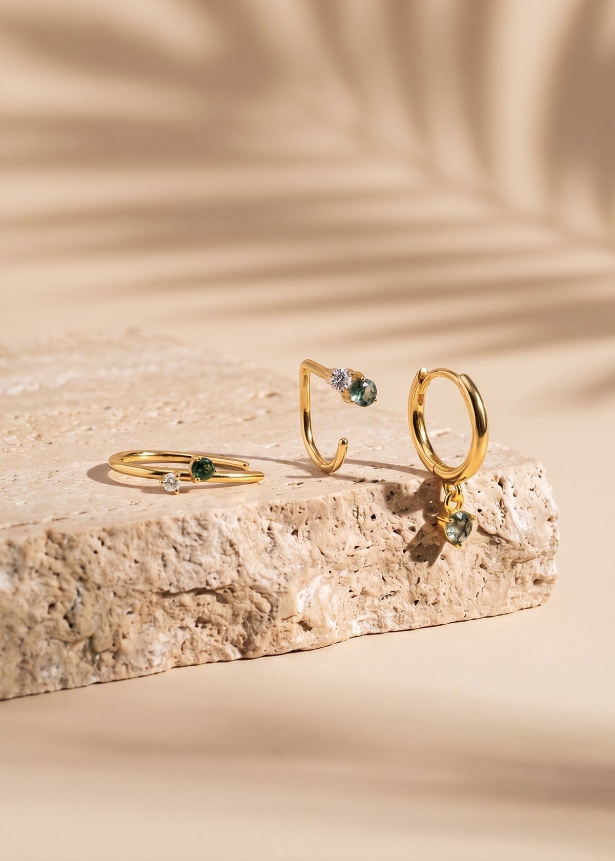 Gold Monet-inspired moss agate hoops standing on a textured stone block