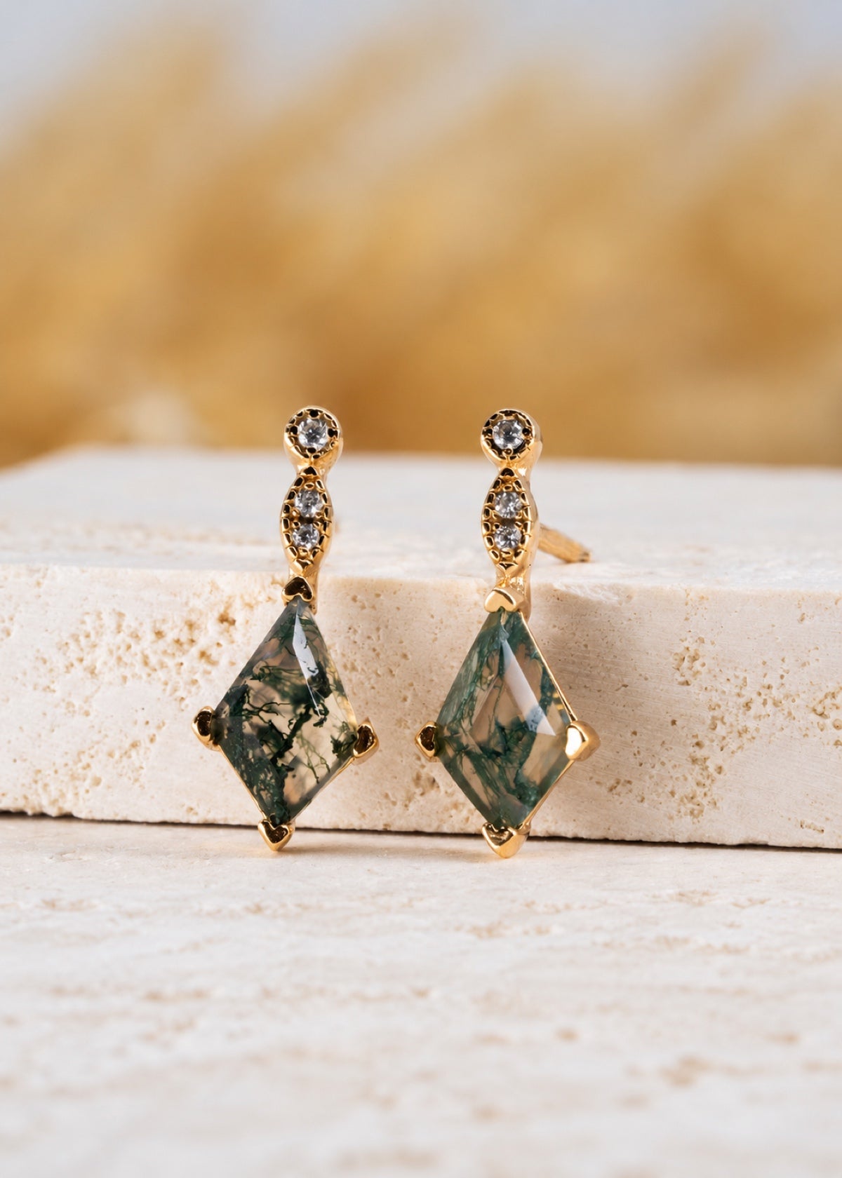 Moss agate earrings displayed upright on a stone ledge