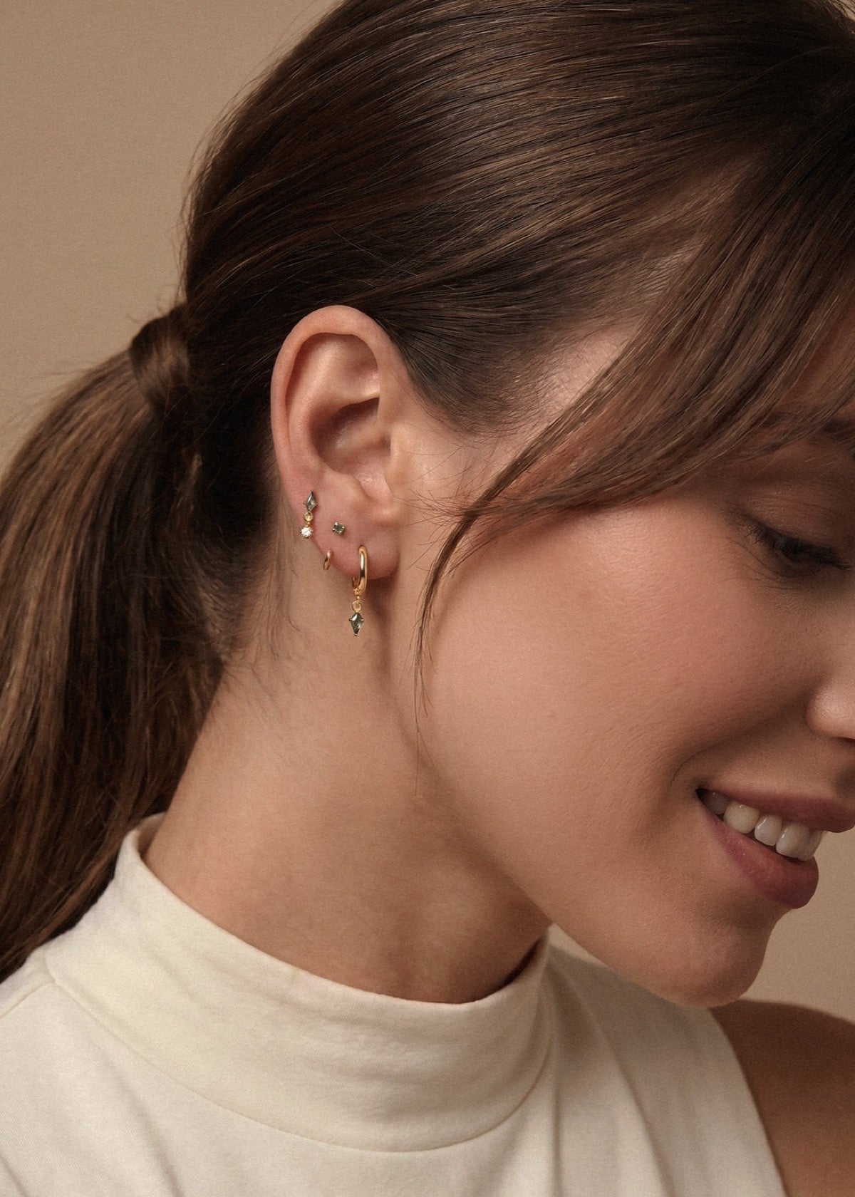 Gold moss agate ear stack worn with a cream turtleneck