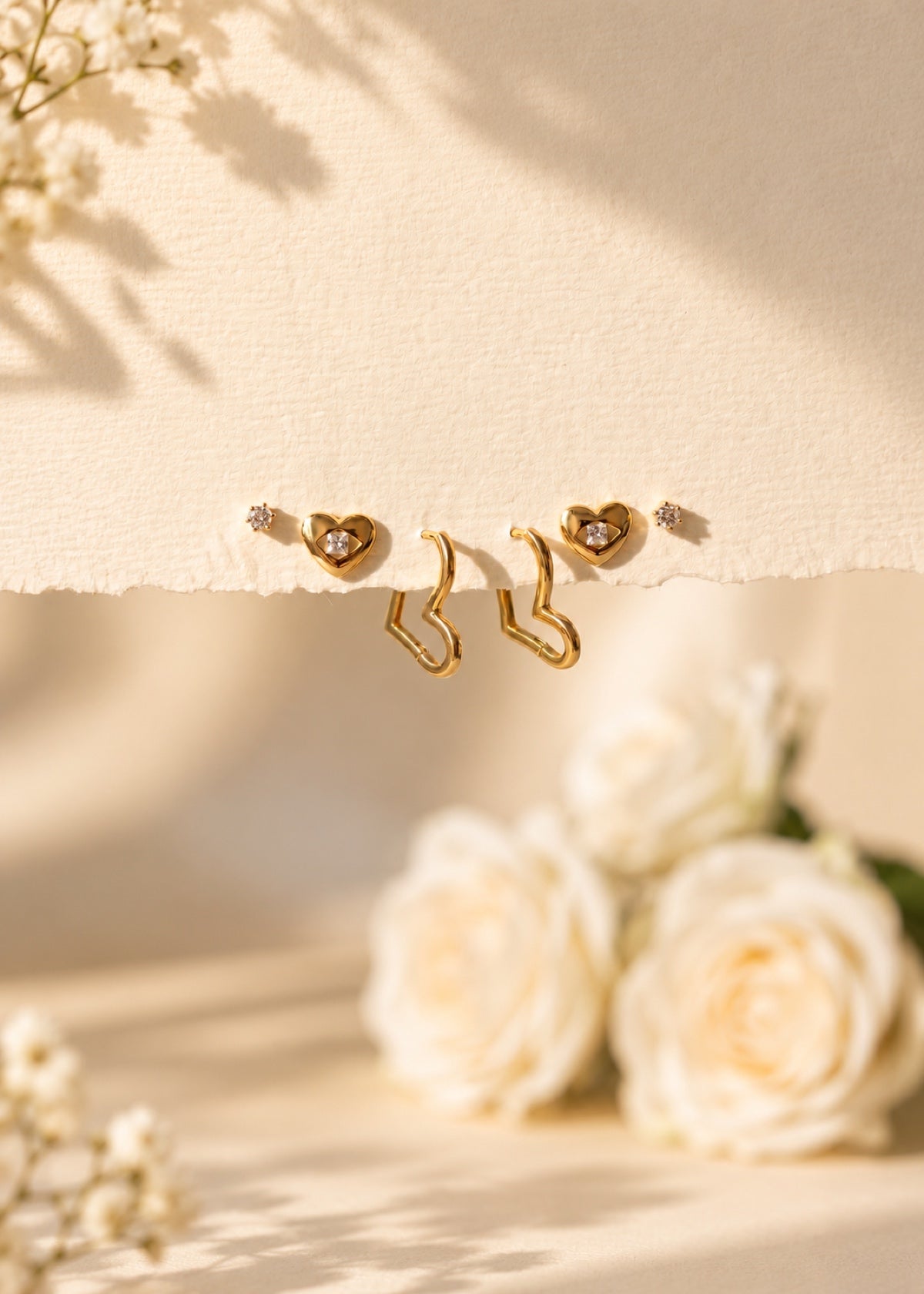 Gold heart CZ studs and angular huggie hoops arranged on a stone ledge
