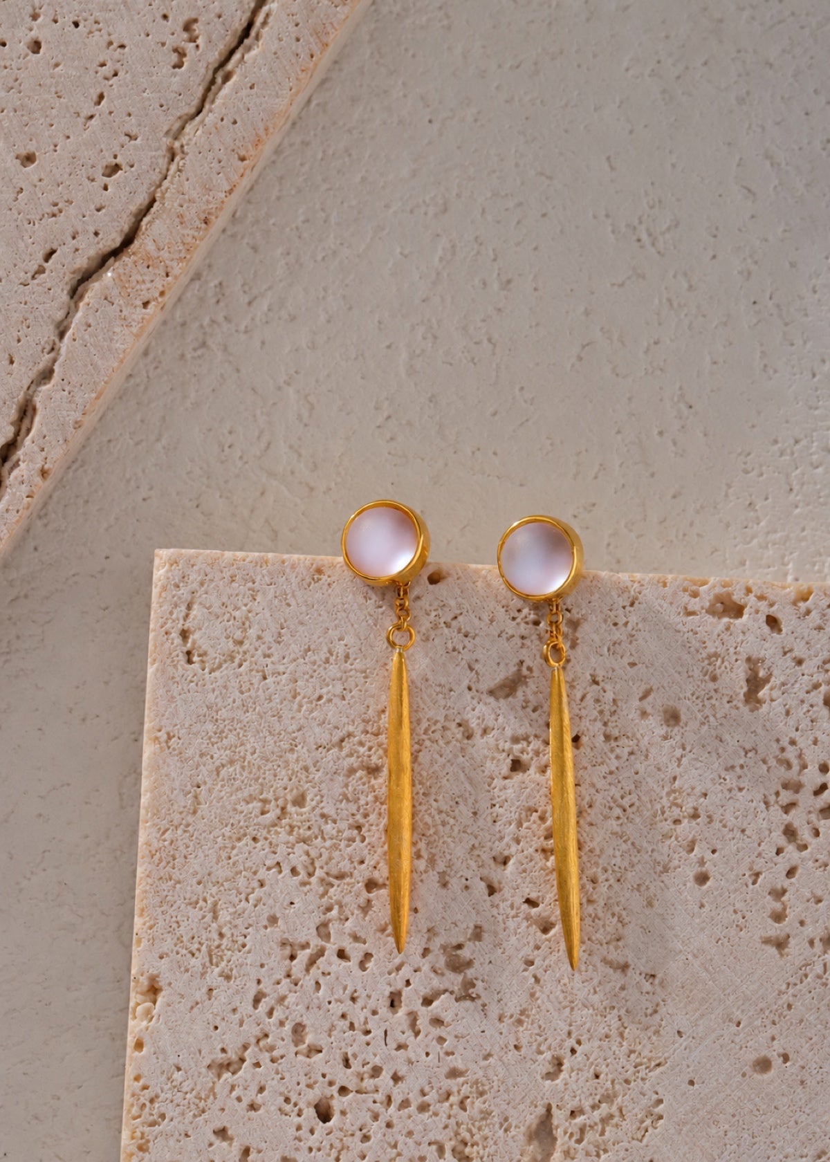 Gold moonstone bar dangle earrings on a stone ledge