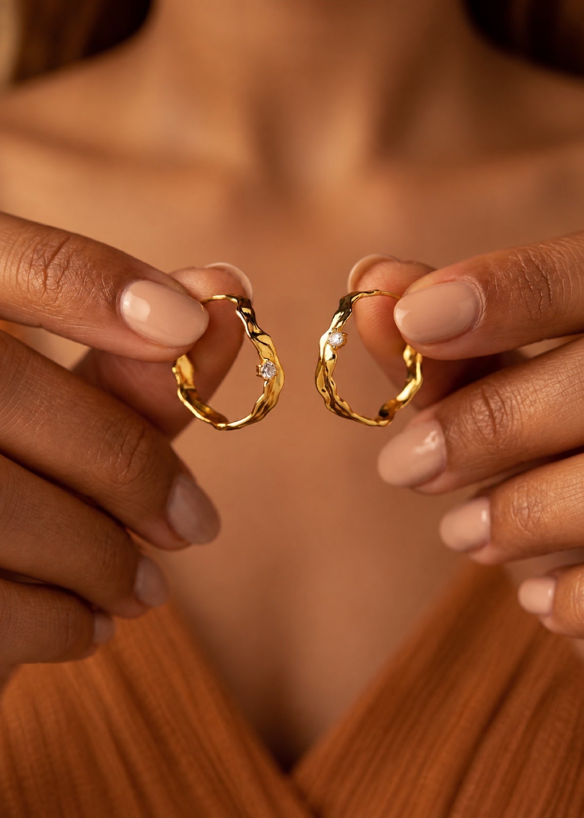 Hands holding a pair of Wave Huggies to show their hoop shape and CZ details
