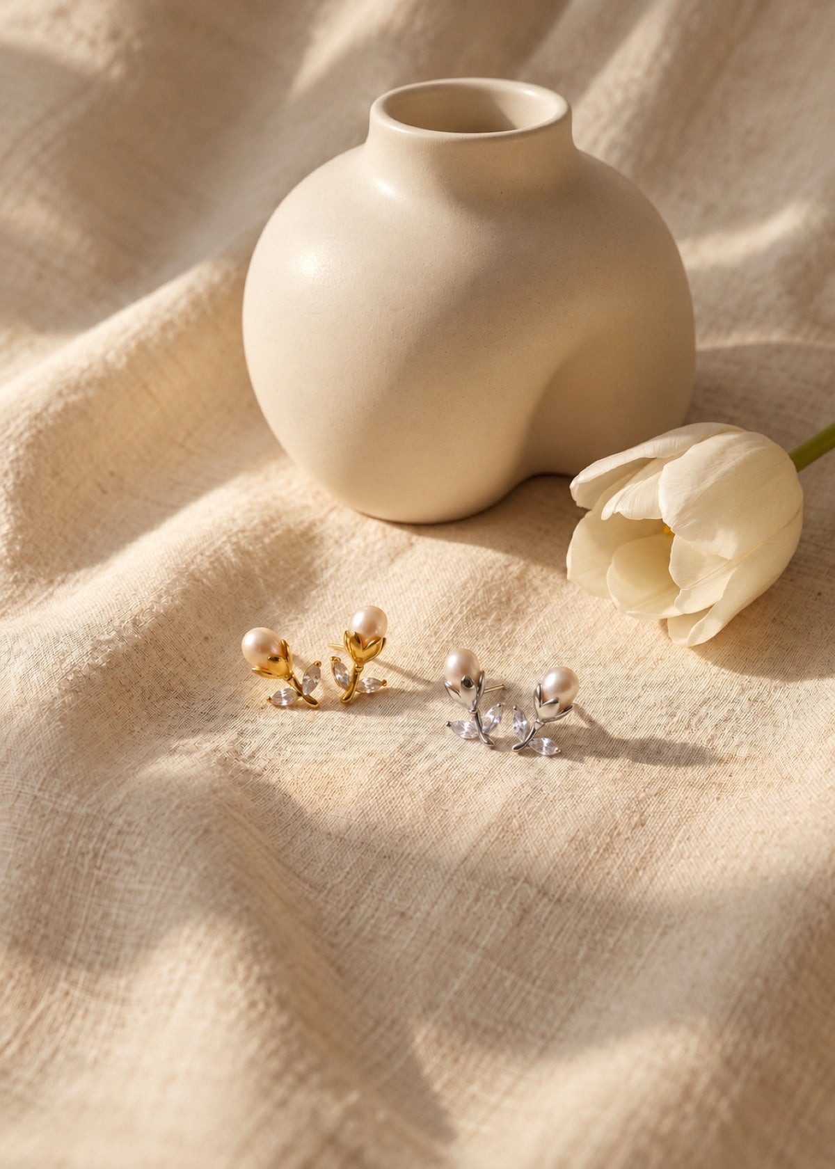 Gold and silver tulip pearl studs on fabric beside a vase