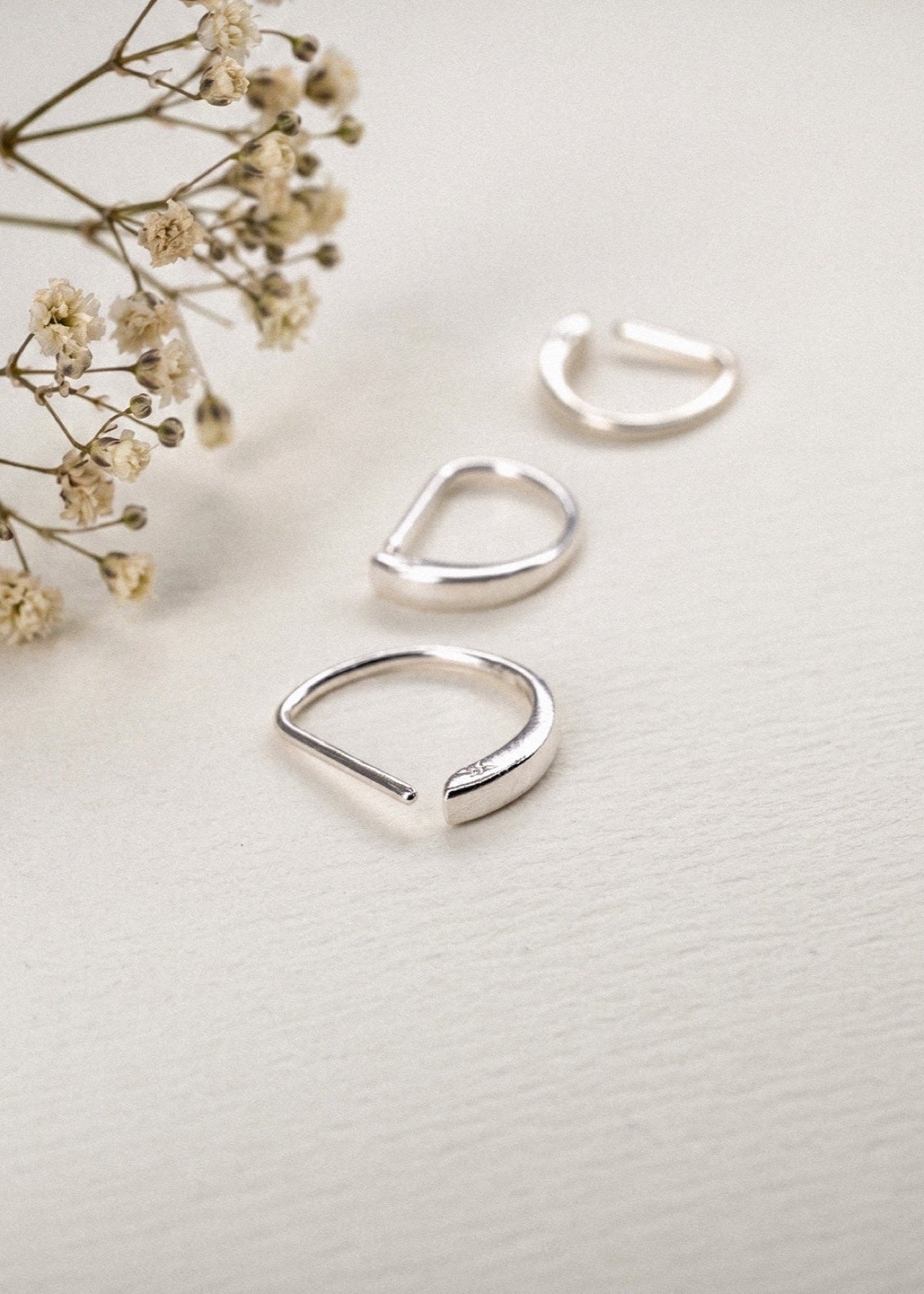 Three sterling silver D Shape sleeper earrings beside dried flowers