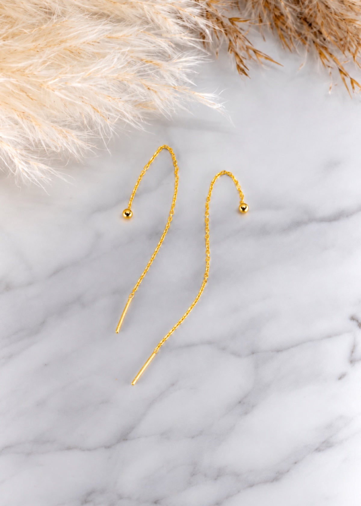 Gold ball threader earrings arranged on a marble surface