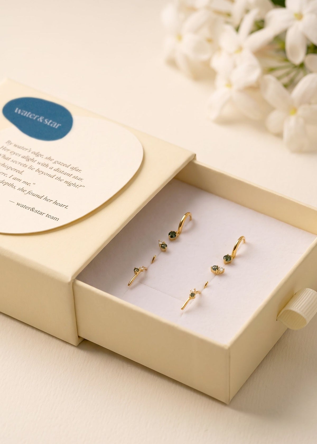 Water & Star gift box containing gold earrings beside flowers