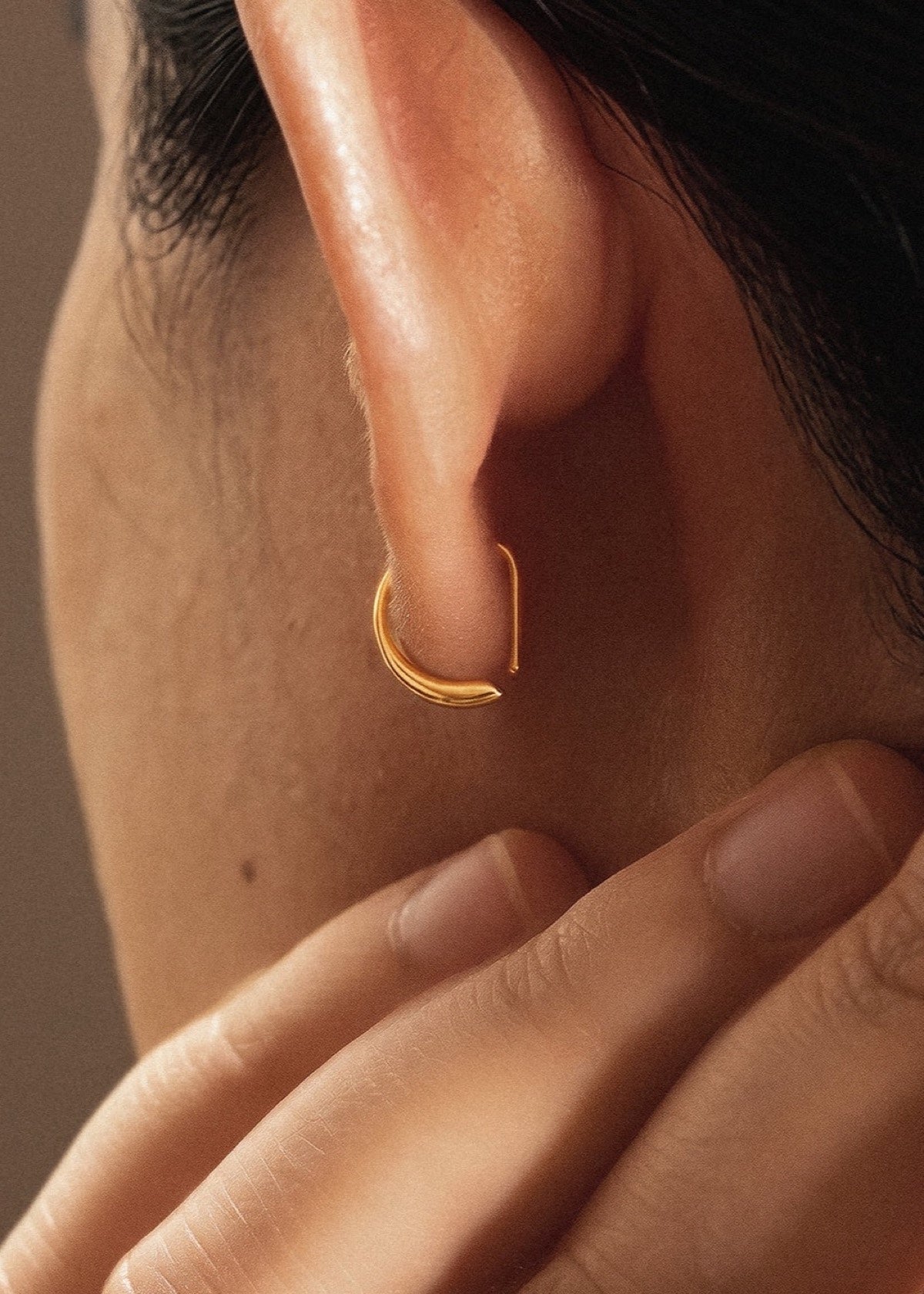 Close-up of a gold D Shape sleeper earring showing its fit around the earlobe